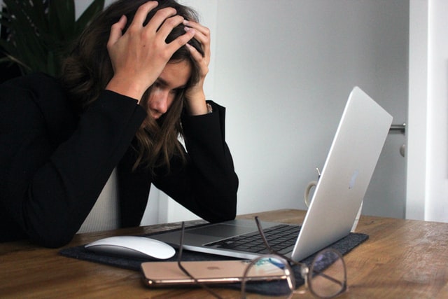 Woman sitting with laptop, hands to the head in frustration
