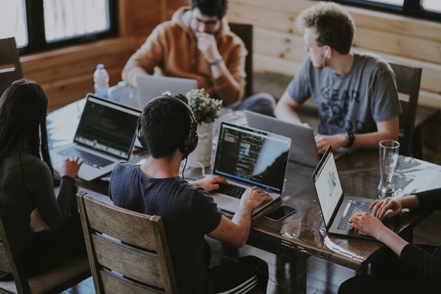 A group of studens sitter together around a table working on their laptops
